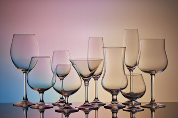 Empty clear glassware. Set of glasses for different alcoholic drinks and cocktails on multicolor gradient background