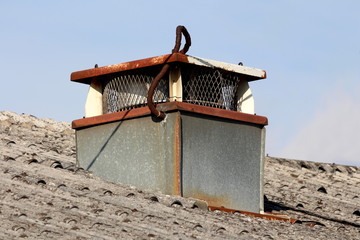 Rectangular rusted chimney with metal mesh protection on all sides covered with partially rusted cover on top of abandoned industrial building