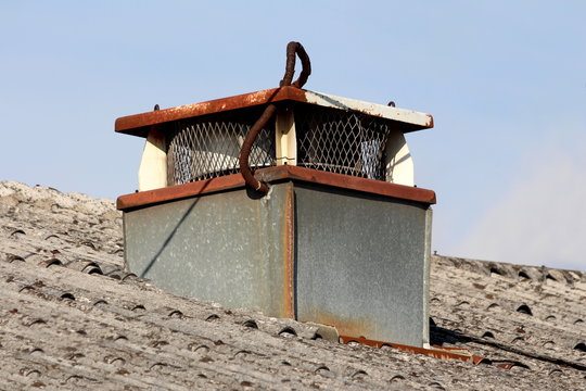 Rectangular rusted chimney with metal mesh protection on all sides covered with partially rusted cover on top of abandoned industrial building