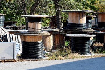 Thick black electrical cable on various sizes industrial wooden cable winding spool drum reels left...