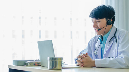 Smiley asia Doctor wears a headset looking notebook laptop to talk and consult with patients health care and medicine with online conferencing system service medical from clinic hospital office cope s