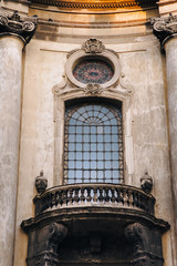 Antique baroque round window framed by decorative stucco with a balcony and balustrade below on a beige wall background. Dominican Cathedral Monastery. Lviv, Ukraine.