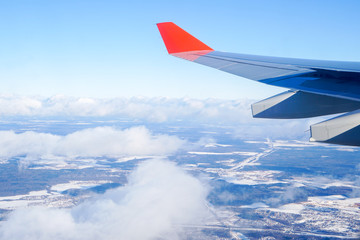 airplane wing with red winglet above the clouds, view of the blue sky from the porthole
