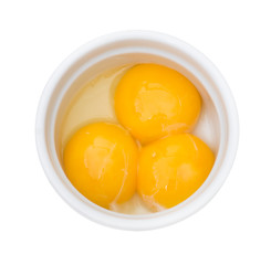 Bright yellow egg yolks in a white bowl on white background