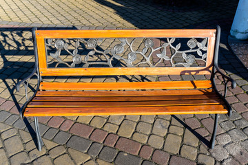 A decorative bench made by hand from wrought metal in the shape of leaves and a wooden seat, standing on a paving stone.