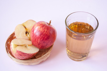 Cut and whole red Apple in a wicker plate and a glass of Apple juice on a pink background