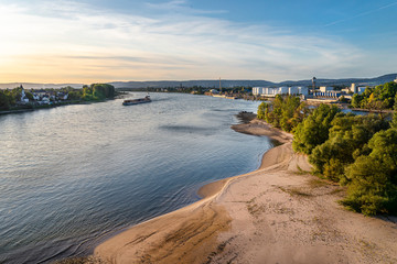 A barge flowing on the river Rhine in western Germany at sunset, the dried river bank visible.