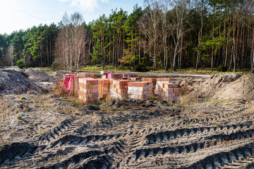 Red bricks for the construction of the house gathered on pallets at the construction site in the field.