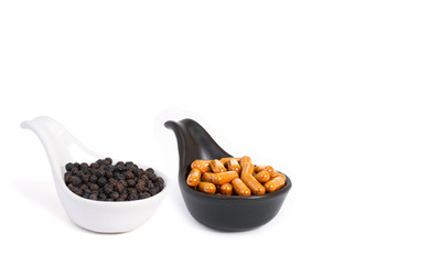 Curcuma capsules and black peppercorns in ceramic spoon isolated on white background. Health benefits and antioxidant food concept.