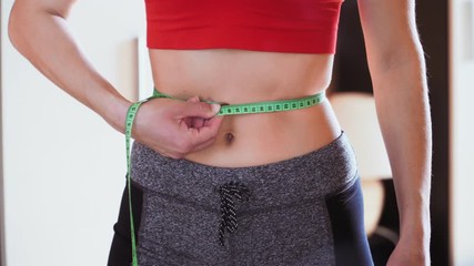 Young athletic slim woman measuring her waist. A girl measures her waistline with a centimeter tape. Healthy lifestyle and proper nutrition. Diet for weight loss