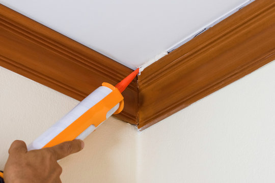 Technician man hand using glue gun or manual caulking gun with polyurethane silicone to repair and fix the wooden cornice with the ceiling. Installation or renovation interior concept. 