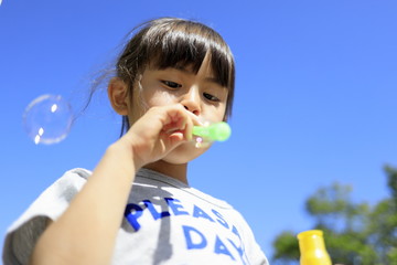 シャボン玉で遊ぶ幼児(5歳児)と青空