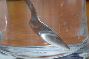 Metal spoon in empty glass cup. Lime stains smeared with water on glass.