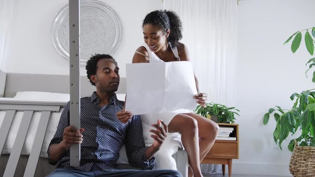 Confused Man Looks At Instructions For Self Assembly Baby Cot Before Pregnant Wife Turns Them Over