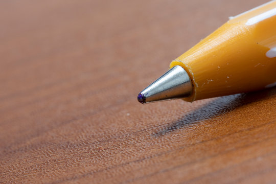 Ballpoint pen nib close-up. It is yellow and brown on the table.
