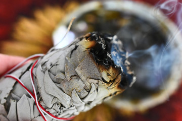A close up image of a hand holding a burning white sage smudge stick. 