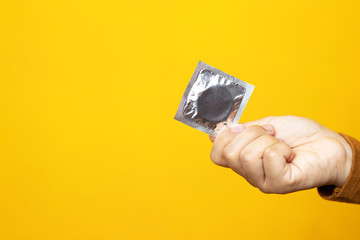 Condom ready to use in female hand on yellow background, give condom safe sex concept on the bed Prevent infection and Contraceptives control the birth rate or safe prophylactic. World AIDS Day,