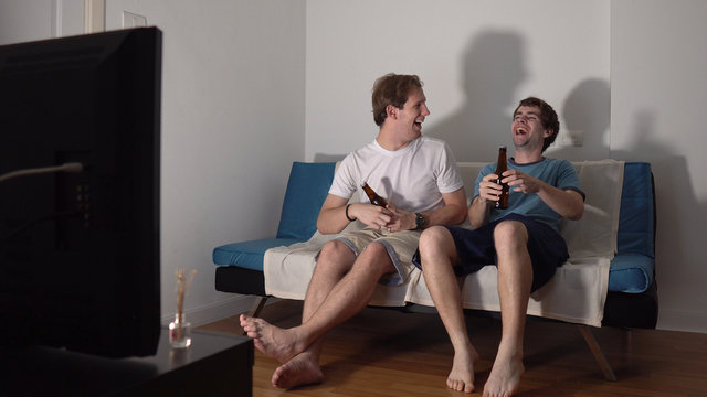 Two Young Adult Male Friends Sitting on Couch and Casually Watching TV