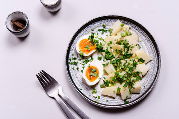 Boiled potatoes with herbs and soft-boiled eggs in a plate on grey concrete background. Selective focus