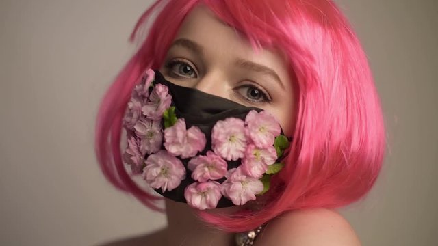 Girl with bright pink hair, anime, in a mask of flowers. Spring, joy, people should wear masks. Fashionable photo of a girl in a mask. Spring, coronavirus, pandemic.