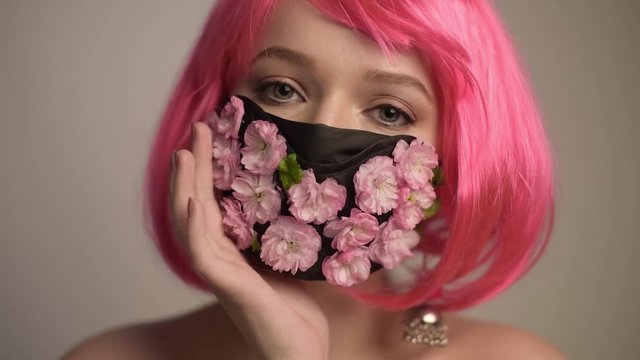 Girl with bright pink hair, anime, in a mask of flowers. Spring, joy, people should wear masks. Fashionable photo of a girl in a mask. Spring, coronavirus, pandemic.