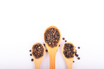 Black peppers on wooden spoon on white background.