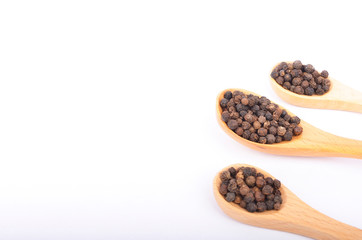 Black peppers on wooden spoon on white background.