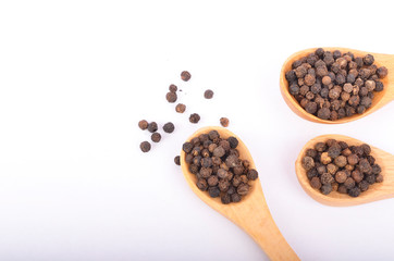 Black peppers on wooden spoon on white background.
