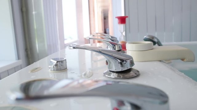 Five metal taps for water are shown close-up. An hourglass is behind. The camera moves from left to right and vice versa. Bright room.


