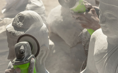 Stone carver using grinding tool to shape white marble and create unique Burmese Buddha statues, in...