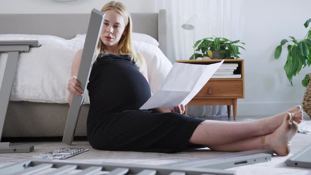 Pregnant Mother To Be Looking At Instructions For Self Assembly Baby Cot In Bedroom