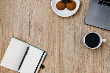 Flat lay of the workplace. Freelance work laptop smartphone and note pad. Morning coffee with cookies. Copy space on wooden background and notepad.