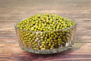 Mung bean in glass bowl on wooden table. The mung bean (Vigna radiata), alternatively known as the green gram, maash, or moong. It is used as an ingredient in both savory and sweet dishes.