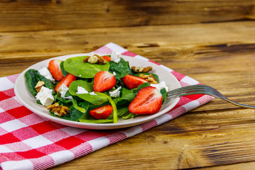 Fresh healthy salad with strawberry, spinach, walnuts and feta cheese on wooden table