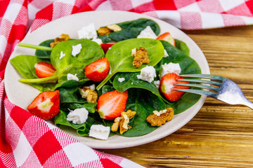 Fresh healthy salad with strawberry, spinach, walnuts and feta cheese on wooden table