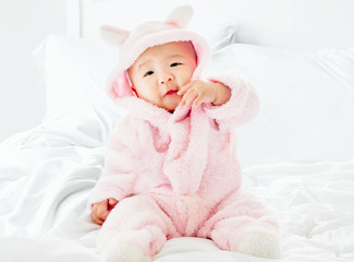 Soft and selective focus A newborn Asian baby boy 4 month smile and happy, Wearing a pink bear suit Sitting on a white bed with the little blue bear