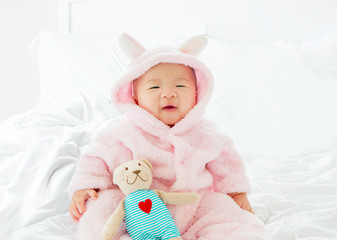 Fototapeta na wymiar Soft and selective focus A newborn Asian baby boy 4 month smile and happy, Wearing a pink bear suit Sitting on a white bed with the little blue bear