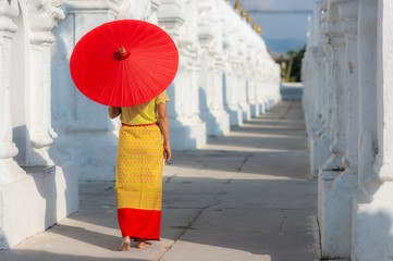 Burmese Asian woman in yellow national costume carrying red umbrella walking  and sightseeing at white Stupas in Kathodaw temple in Mandalay,Myanmar