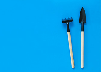 Garden rake and shovel with wooden handles on a blue background.