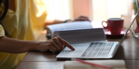 Closeup woman relaxing and using a computer laptop while sitting at the wooden working desk over comfortable living room windows as background. Student tutoring and online learning concept.