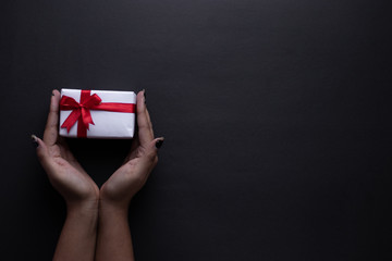 White gift box with red ribbon, black background flat lay for stock image