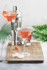 Classic alcoholic cocktail Manhattan with american bourbon, red vermouth, bitter, ice and cocktail cherry in glass, tools, gray bar counter background, copy space, selective focus