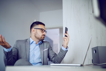 Confused caucasian handsome unshaven classy businessman in suit and with eyeglasses sitting in his...