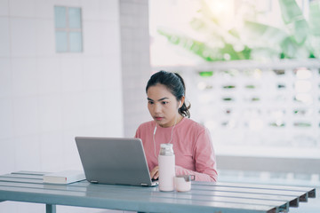 Portrait of a young Asian business woman working with laptop at home in house corridor and garden during Coronavirus spreading.  Adult Asian female learner studying online at home.