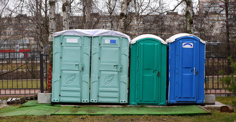 Blue and green plastic compact mobile toilet near lattice fence