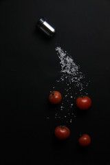 four tomatos, salt shaker and pouring salt isolated on black background. Concept of flying food