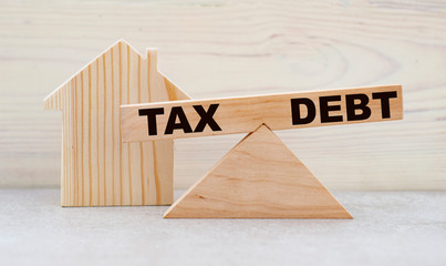 The concept of the balance of words between TAX and DEBT on wooden scales on a light background