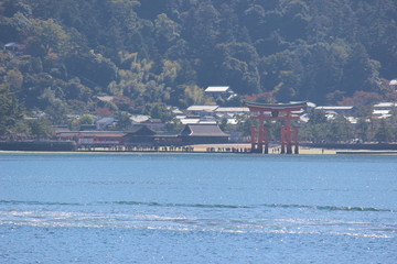 Looking at Miyajima island from the ferry. Floating red giant Grand O-Torii gate stands in bay...