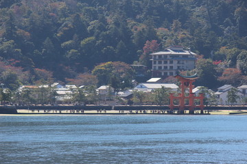 Fototapeta na wymiar Looking at Miyajima island from the ferry. Floating red giant Grand O-Torii gate stands in bay beach at low tide on sunny day, Hiroshima City, Hiroshima Prefecture, Japan. 厳島神社
