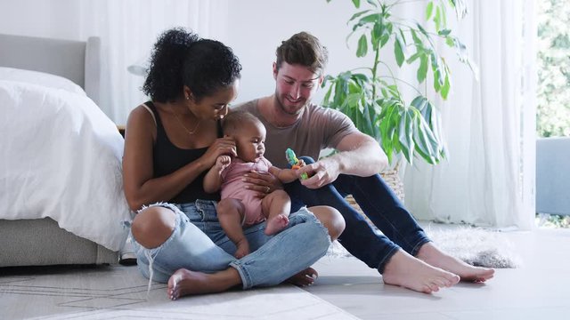 Loving Parents Playing With Baby Daughter Sitting On Floor In Bedroom